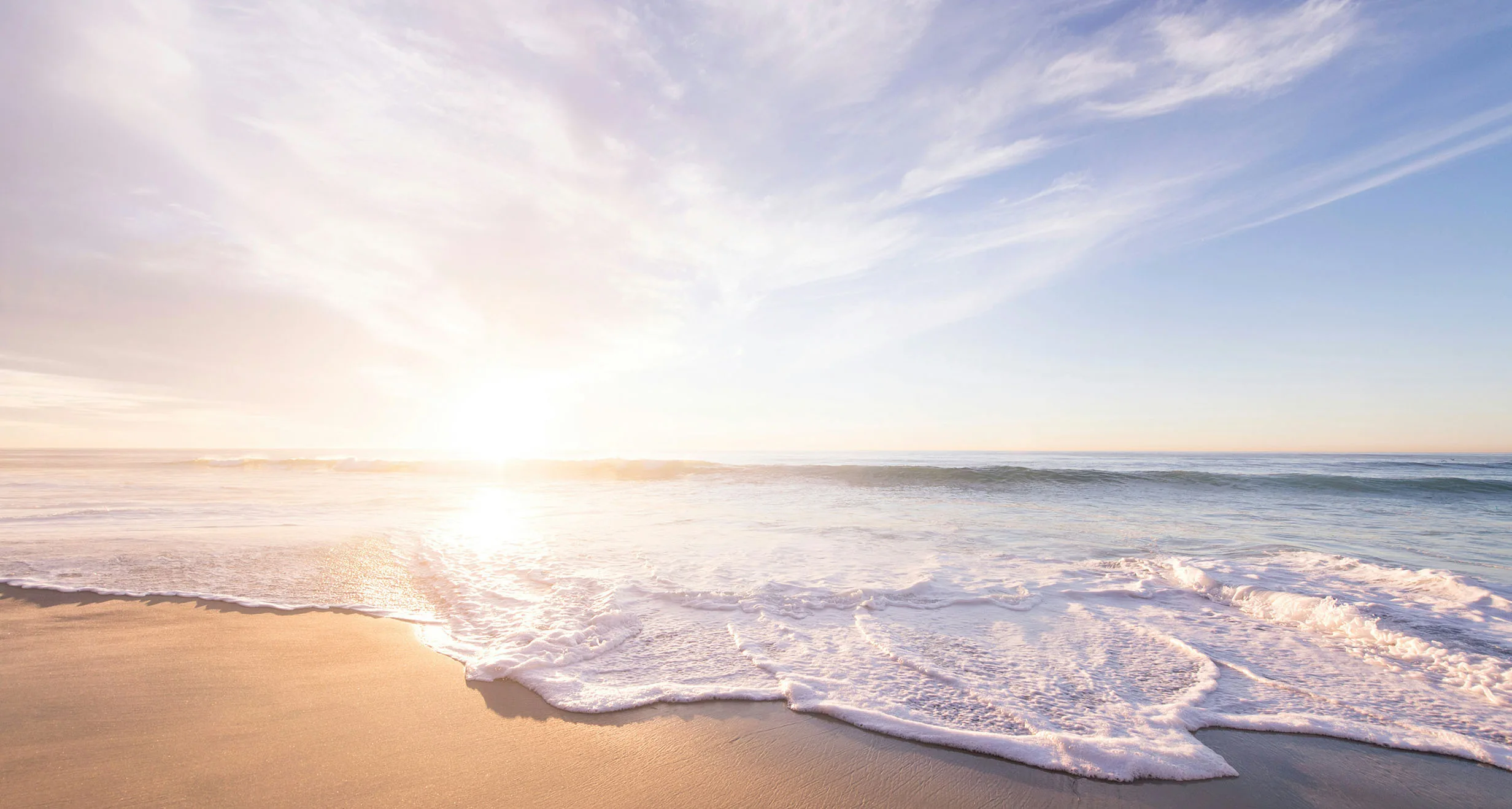 Wellensaum am Sandstrand in ruhiger, warmer Abendstimmung mit Sonne und Wolkenhimmel – Symbolbild für Paarberatung und buddhistische Psychologie